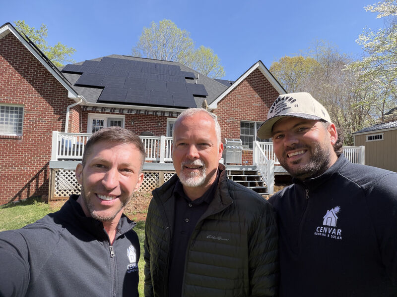 Solar team with homeowner in front of rooftop solar panels on brick home